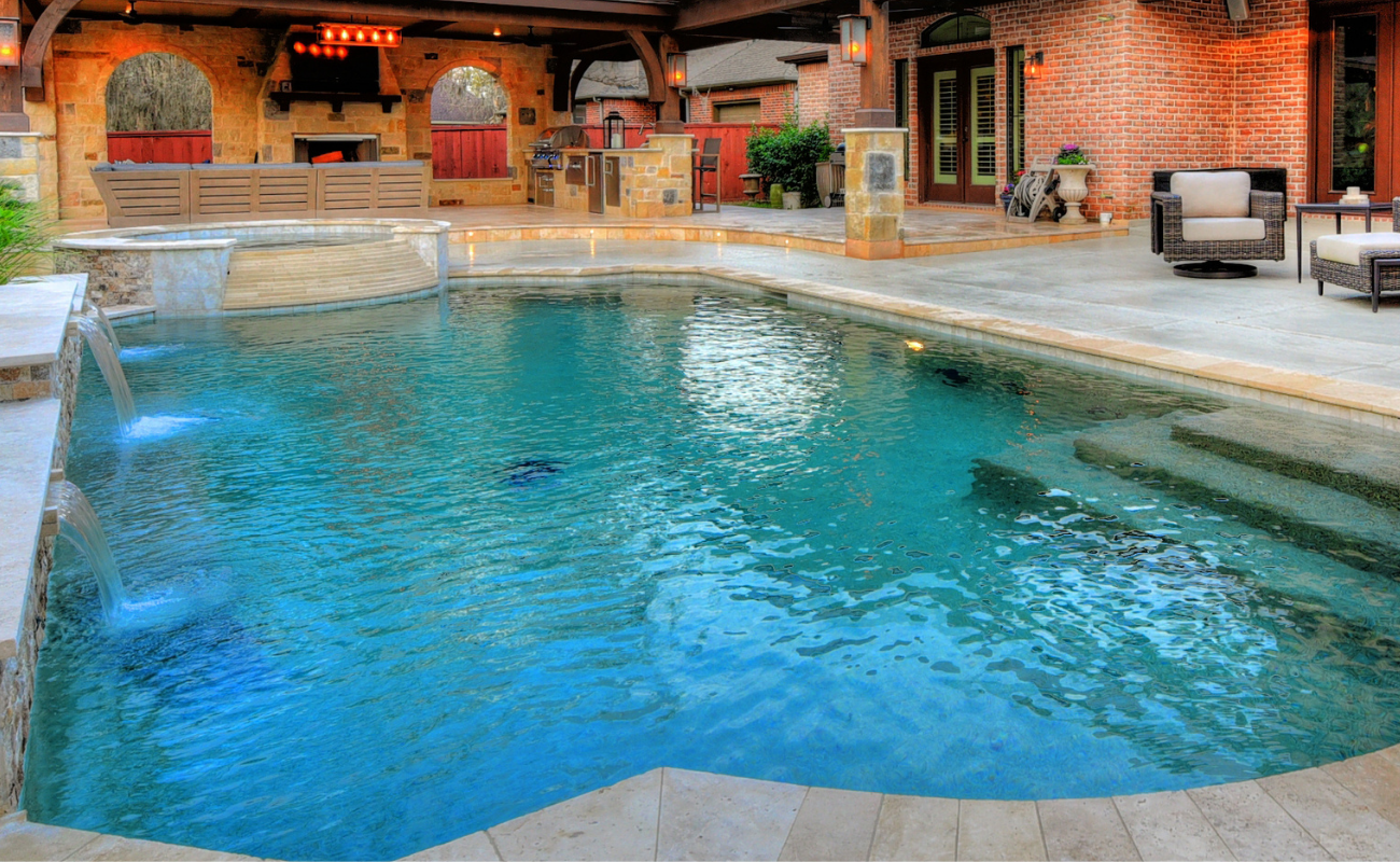 High-end luxury pool design featuring a raised spa, stone water features, and a covered patio kitchen.