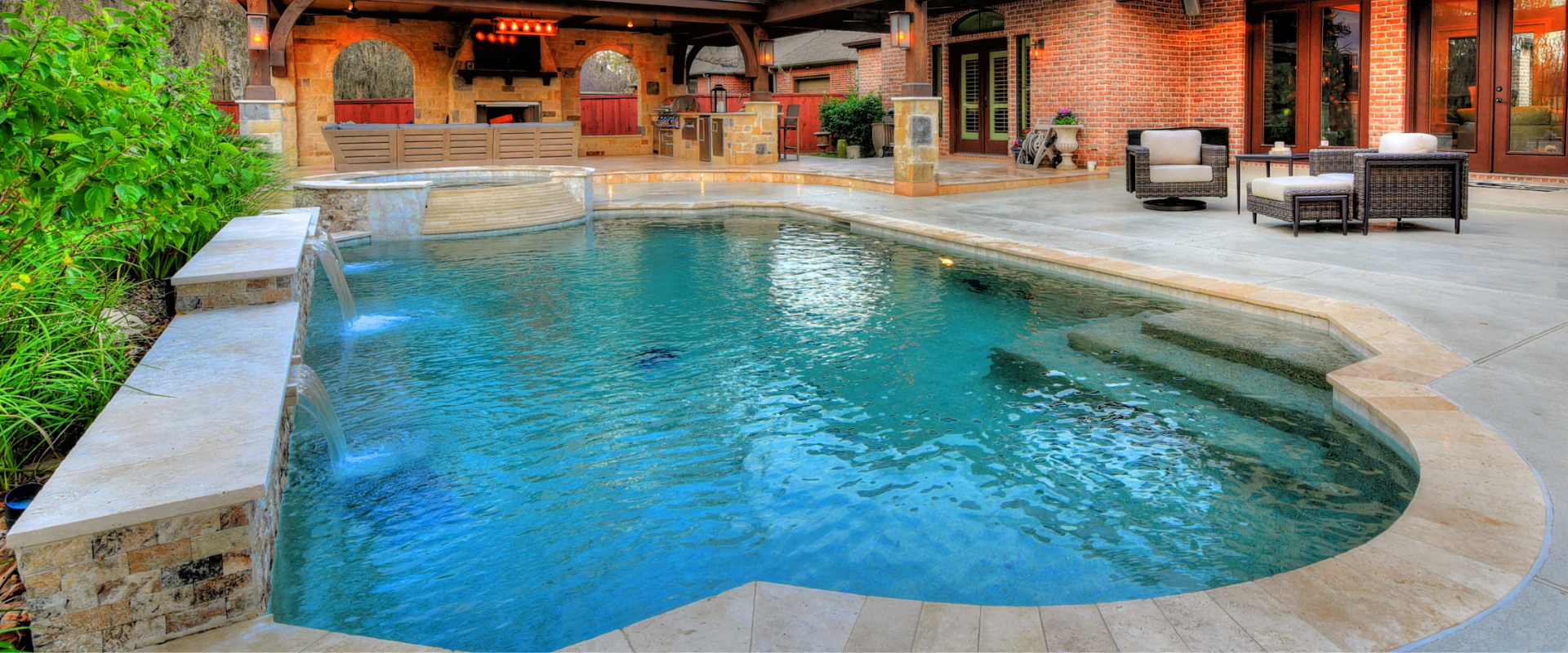 High-end luxury pool design featuring a raised spa, stone water features, and a covered patio kitchen.