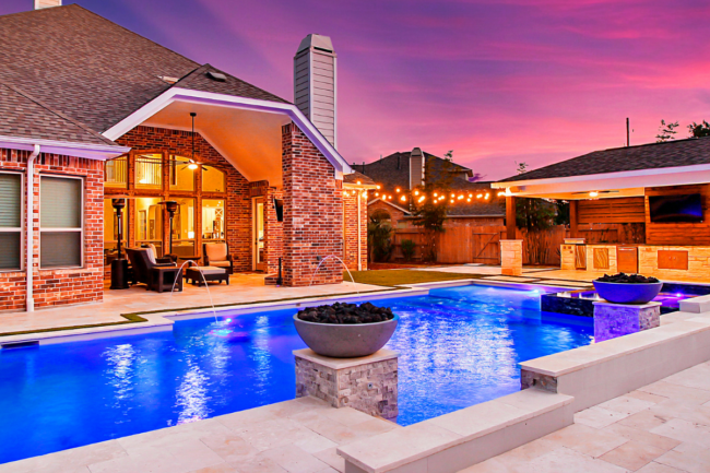 Renovated backyard featuring modern pool renovation ideas like LED lighting, fire bowls, and a pavilion.