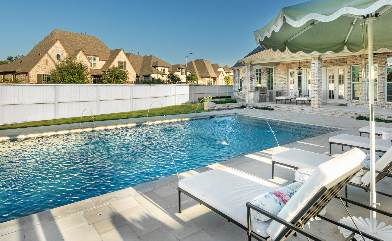 Custom gunite pool with deck laminar jets, sun loungers, and patio umbrellas in a luxury backyard.