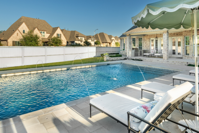 Custom gunite pool with deck laminar jets, sun loungers, and patio umbrellas in a luxury backyard.