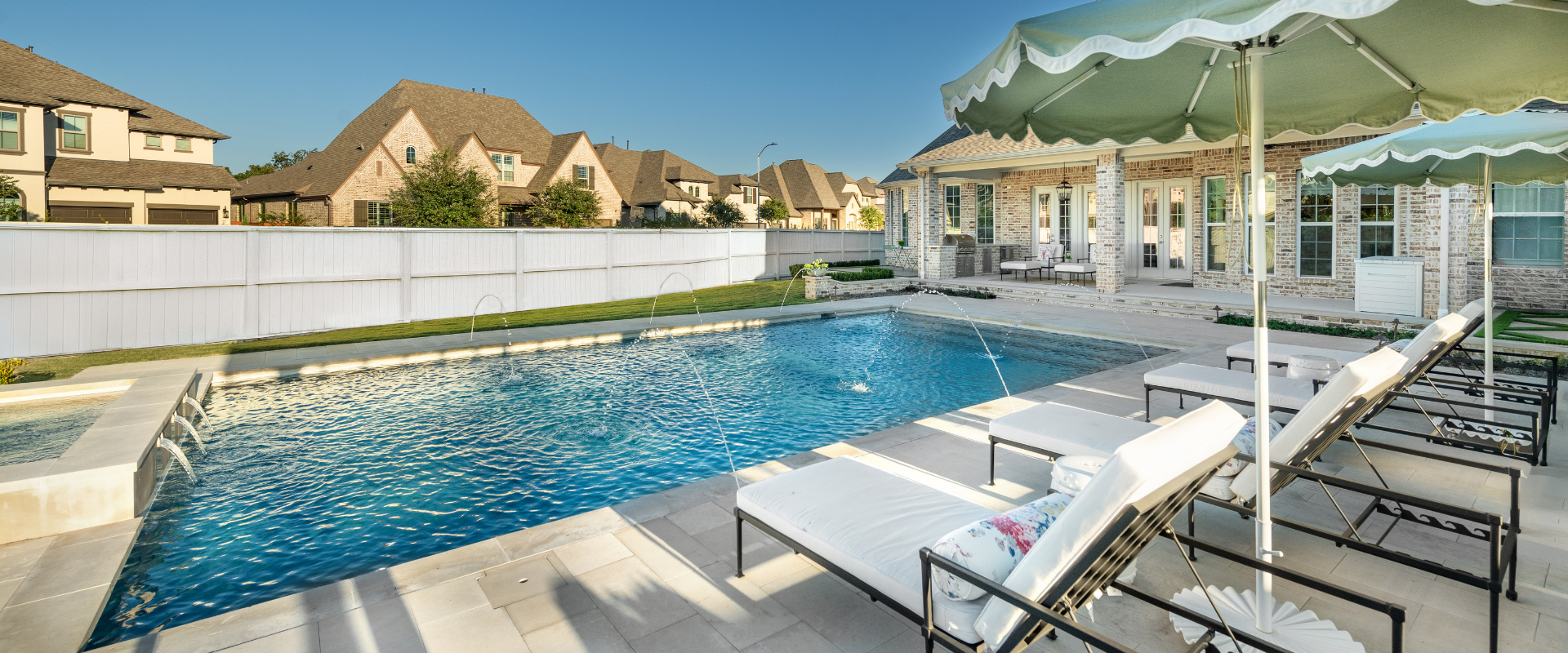 Custom gunite pool with deck laminar jets, sun loungers, and patio umbrellas in a luxury backyard.