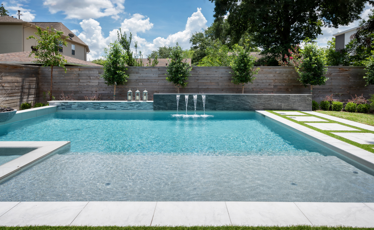 Modern remodeled geometric pool with sheer descent water wall, integrated spa, fire bowl, and stone patio steppers.