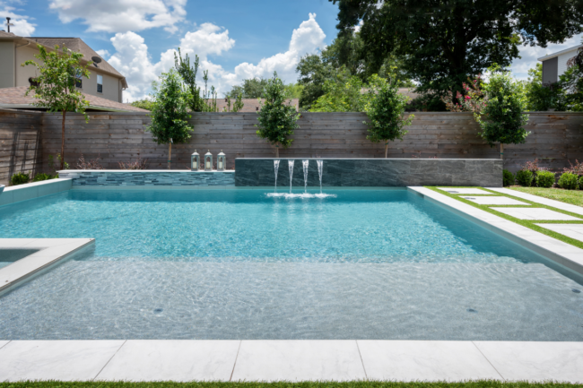 Modern remodeled geometric pool with sheer descent water wall, integrated spa, fire bowl, and stone patio steppers.
