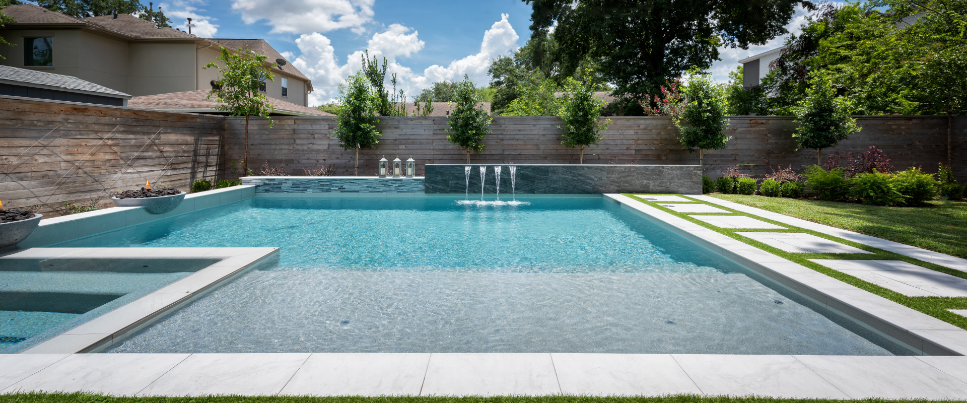Modern remodeled geometric pool with sheer descent water wall, integrated spa, fire bowl, and stone patio steppers.
